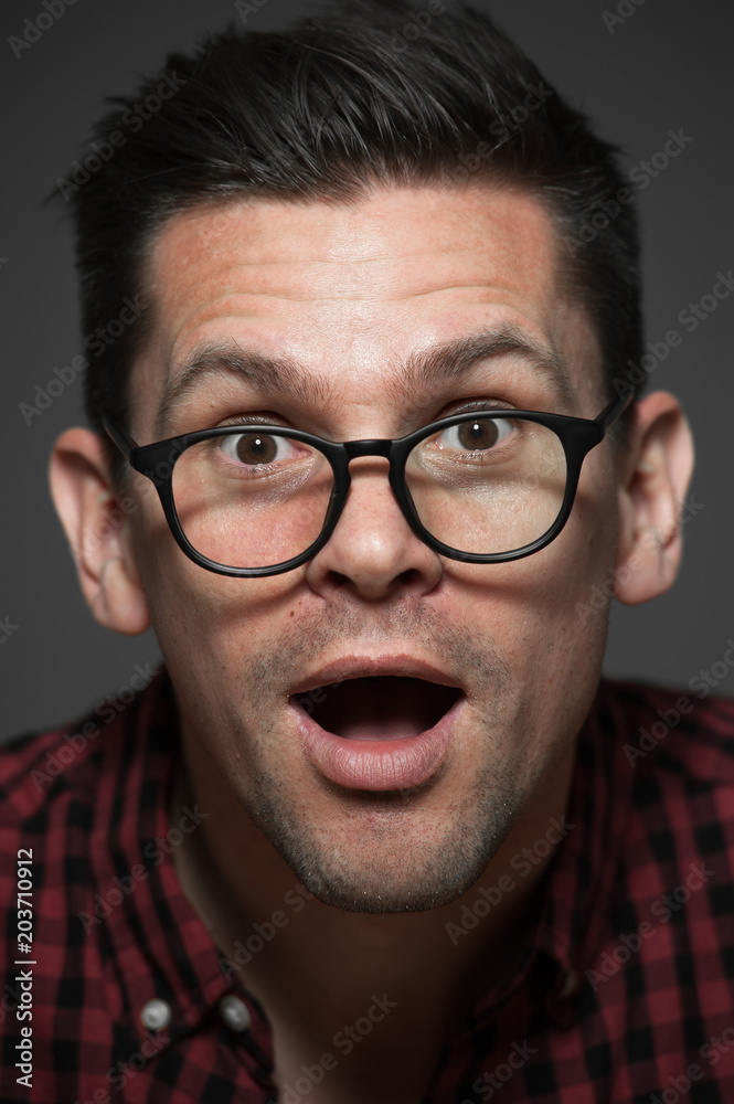 Portrait of cute young hipster man in plaid shirt and glasses showing various emotions on gray background