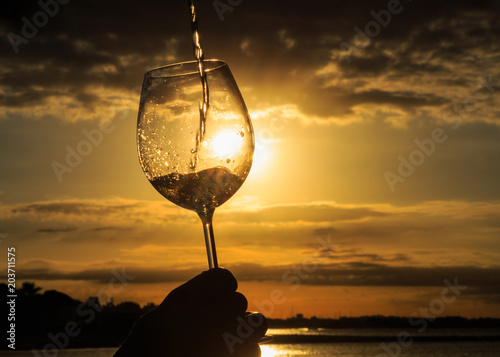 Female hand with a glass of white wine on the background of a beautiful sunset.  Travel vacations concept.