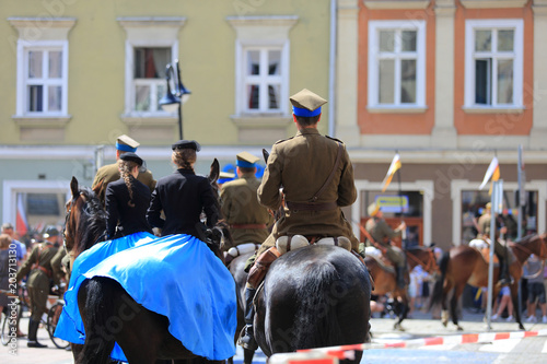 Kobiety w niebieskich sukniach i Żołnierze Wojska Polskiego na koniach.