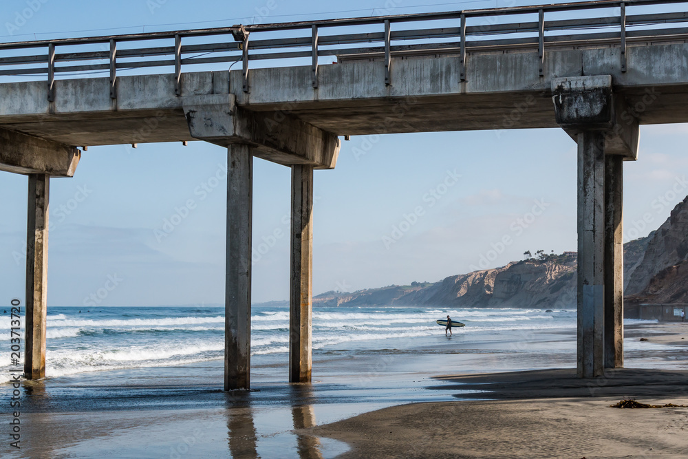A lone male surfer carries a surfboard out to sea near a concrete pier in La Jolla, California A lone male surfer carries a surfboard out to sea near a concrete pier in La Jolla, California