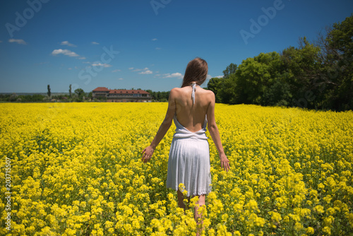 Girl in a white dress with an open back in a canola field under the blue sky