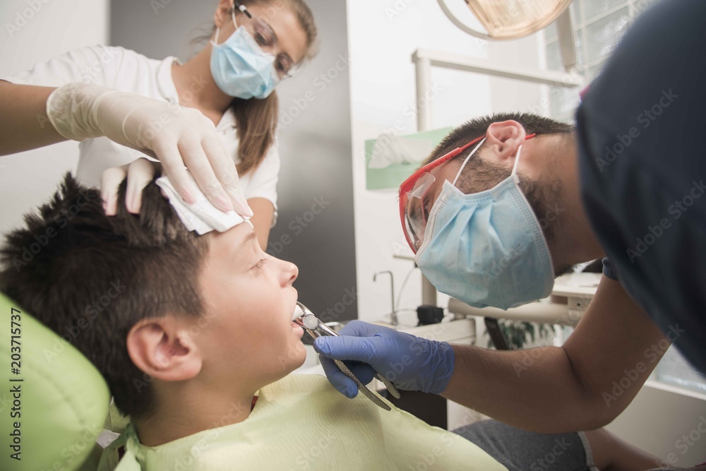 Fototapeta premium A boy having his tooth removed is being comforted by a nurse at the dentist office - oral hygiene health care concept