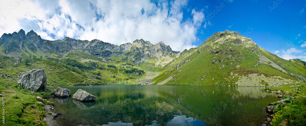 Panorama of clear calm mountain lake in summer day