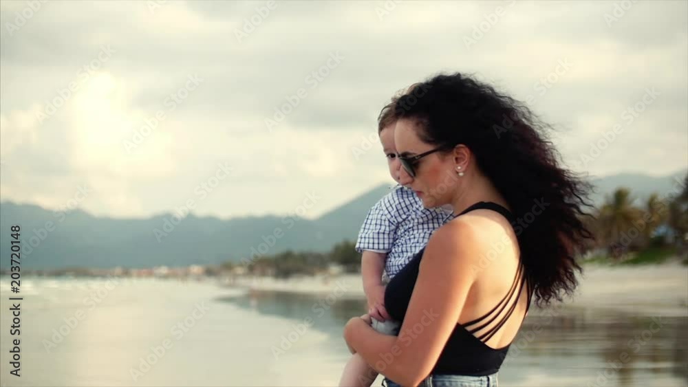 Young family, a mother carrying a son in her arms. A happy family walking along the seashore. Young family, a mother carrying a son in her arms. A happy family walking along the seashore.