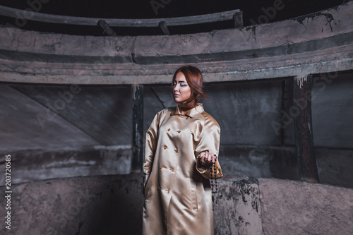 Abstract photo of a beautiful young woman in a beige silk coat against a background of concrete walls of an underground city station with cherries in hand.