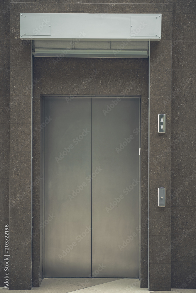 Fototapeta premium Close up grey lift metal door locating in urban building