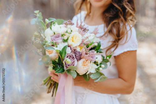 Woman in white dress holding bouquet of flowers in the forest. Bride. Wedding. Marriage.