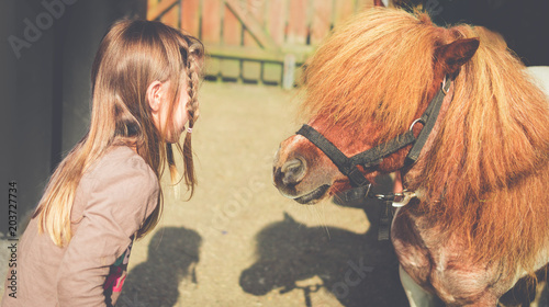 Schilderij op canvas Girl Child Talking to Cute Miniature Horse with Mane Covering Eyes
