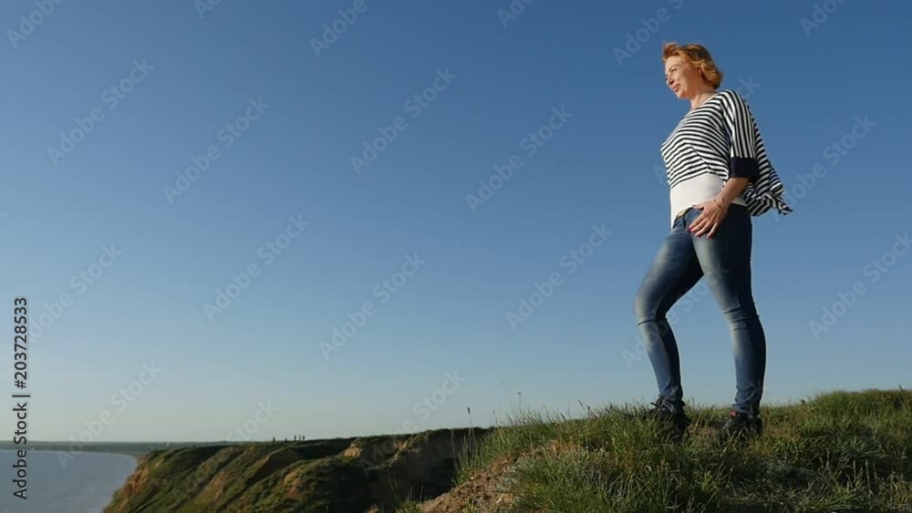 Profile of a cheery blond woman in a striped navy blouse smiling happily and looking at the Black Sea on a sunny day in summer in slow motion Profile of a cheery blond woman in a striped navy blouse smiling happily and looking at the Black Sea on a sunny day in summer in slow motion