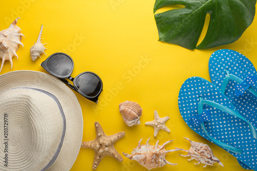 A female hat with round sunglasses and seashells, and beach slippers on a yellow background. Top view with a place for inscription or advertising
