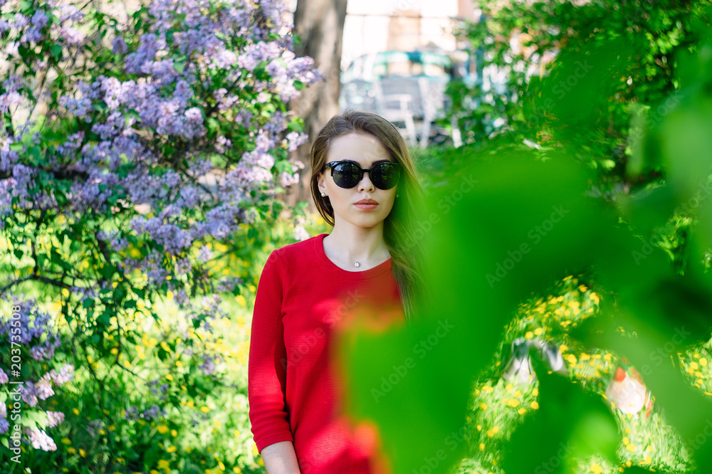 The girl in the spring dressed in a red sweater is around a blue lilac. The girl in the spring dressed in a red sweater is around a blue lilac.