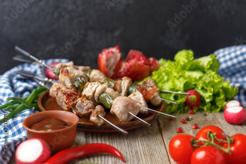 Juicy delicate kebabs of pork on skewers laid out on a dish and fresh vegetables. Still life on a wooden background with textiles. Close-up.