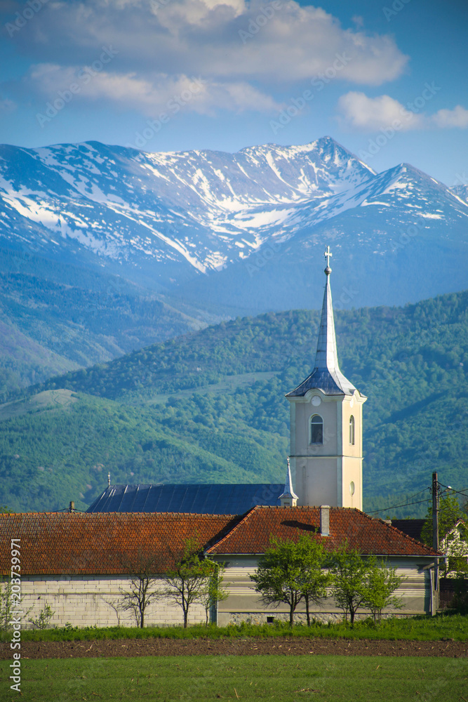 White church tower with corn field foreground and Retezat mountains background in Hunedoara county, Romania