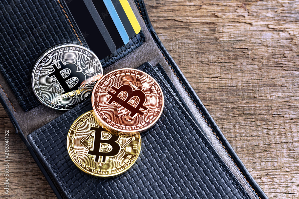 Bitcoins placed into leather wallet on the wooden table. Virtual money or cryptocurrency concept. Bitcoins placed into leather wallet on the wooden table. Virtual money or cryptocurrency concept.