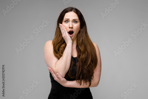 Emotional plus size model standing in studio with open mouth screaming showing despair on gray background