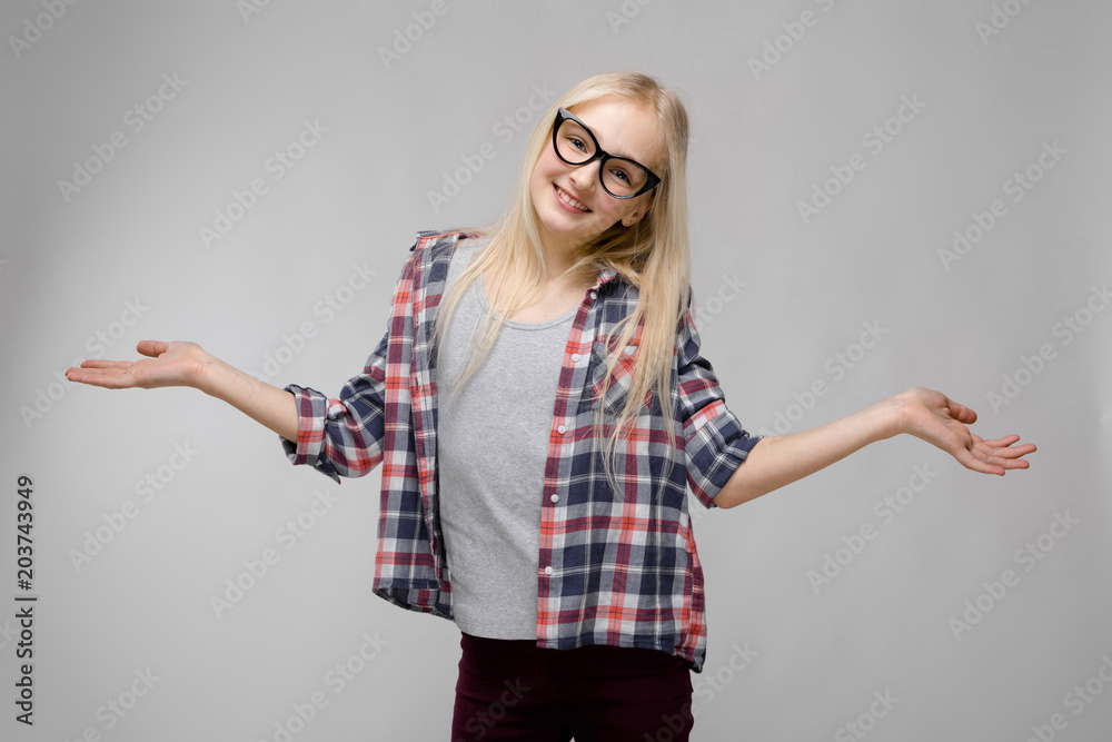 Beautiful teen girl with long hair and wearing glasses. A teenage girl in a plaid shirt and a gray T-shirt. A teenager girl smiles and spreads her arms out to the sides Beautiful teen girl with long hair and wearing glasses. A teenage girl in a plaid shirt and a gray T-shirt. A teenager girl smiles and spreads her arms out to the sides