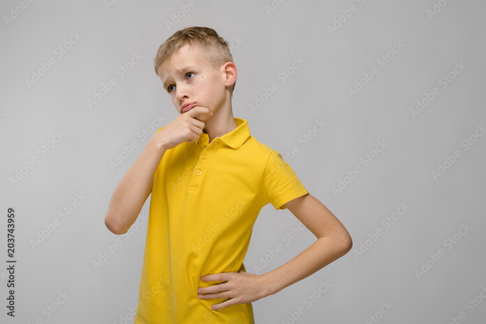 Portrait of cute little blonde caucasian boy in yellow t-shirt unsure puzzled on gray background Portrait of cute little blonde caucasian boy in yellow t-shirt unsure puzzled on gray background