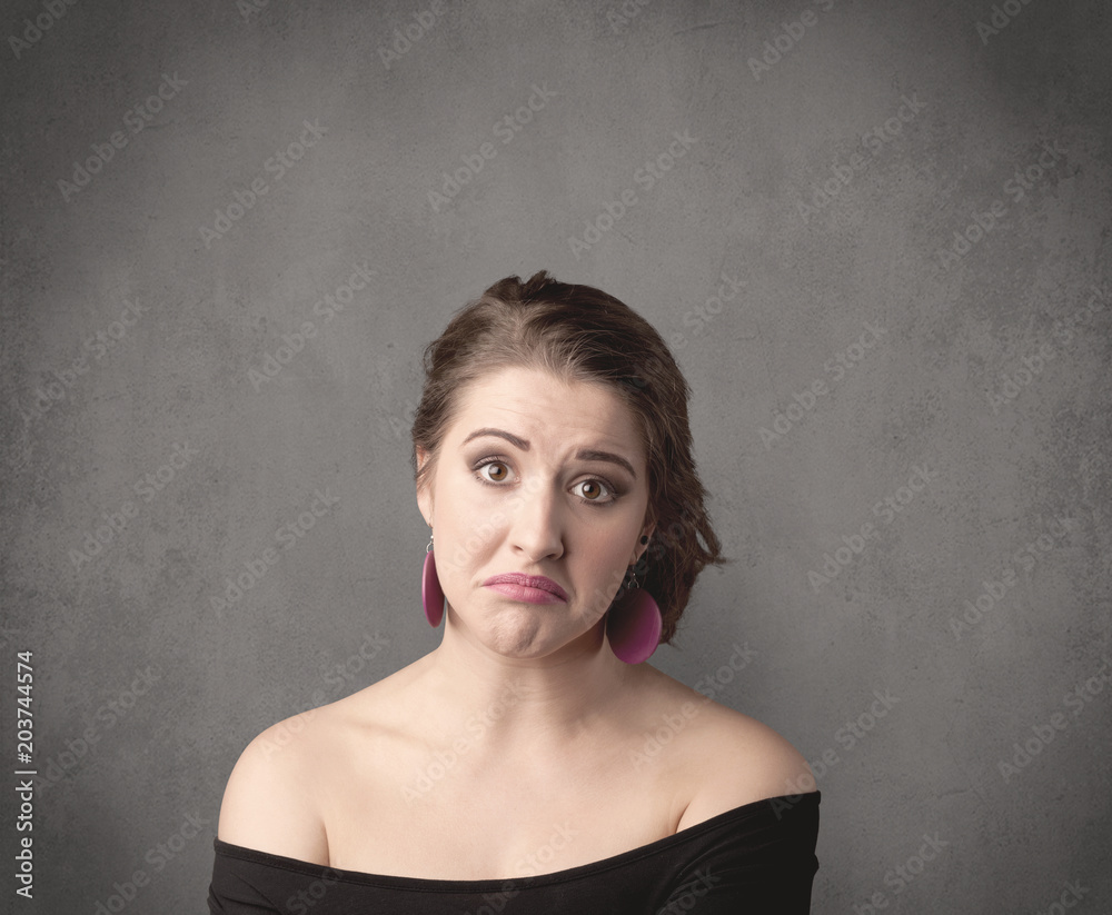 A pretty young teenage girl standing in front of a grey clear empty urban wall background concept while making funny faces. A pretty young teenage girl standing in front of a grey clear empty urban wall background concept while making funny faces.
