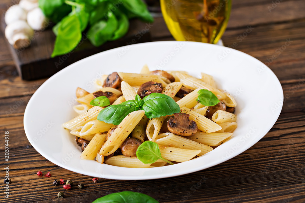 Vegetarian Vegetable pasta penne  with mushrooms  in white bowl on wooden table. Vegan food.