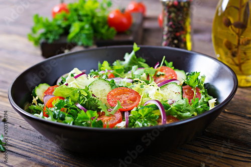 Salad from tomatoes, cucumber, red onions and lettuce leaves. Healthy summer vitamin menu. Vegan vegetable food. Vegetarian dinner table.