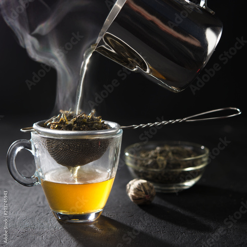 Process brewing tea,tea ceremony,Cup of freshly brewed yellow or green herb tea,warm soft light, dark mood.Hot water is poured from the kettle into a cup with tea leaves.