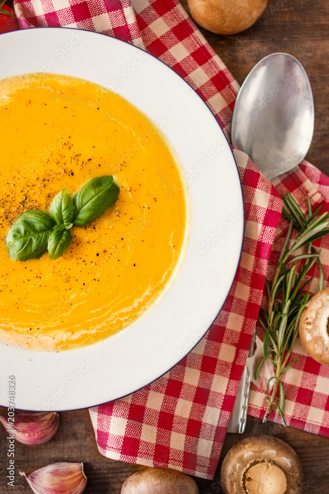 Squash Soup with herbs. Cream soup with  Pumpkin and Carrot  on Red classic Checkered tablecloth on wooden rustic table. Top view. Copy space.