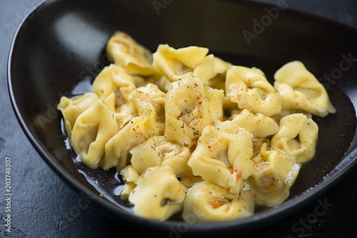 Close-up of a black bowl with tortellini in bouillon, selective focus, horizontal shot