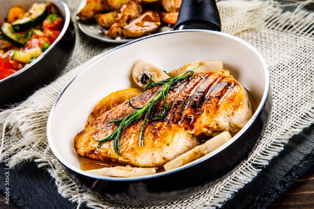 Roast chicken breast with potatoes and vegetables on wooden background
