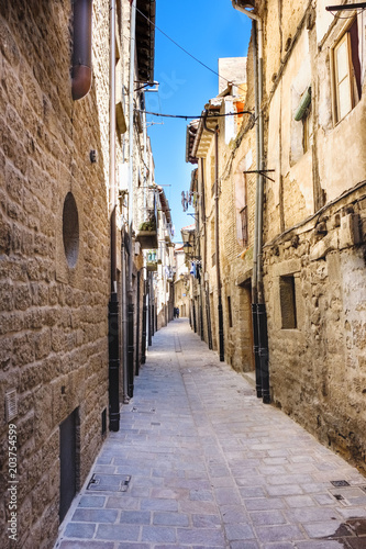 Narrow alley with floor of stone slabs and old houses of stone facades and iron balconies, typical of the north of Spain in the old part of the town called Laguardia in Alava (Spain) © peizais
