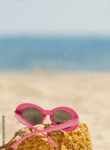 Sunglasses of pink color on the beach.