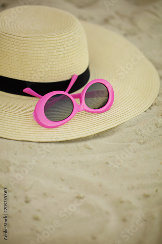 Sunglasses of pink color and hat on the beach.