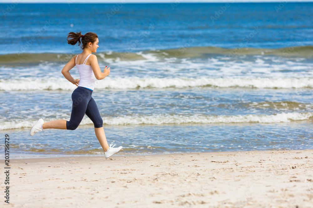 Young woman running, jumping on beach