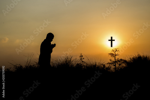Silhouette man praying in front of cross with faith and belief