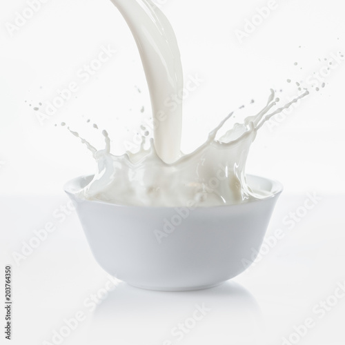 Foto Milk pouring with splashes in white bowl on white background