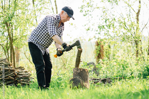 Senior man with axe chopping wood. Elderly arborist man working in garden. Active retirement concept.