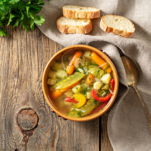 Bright spring vegetable dietary vegetarian soup. Top view, brown rustic wood background, linen napkin.