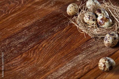 Conceptual still-life with quail eggs in hay nest over dark wooden background, close up, selective focus