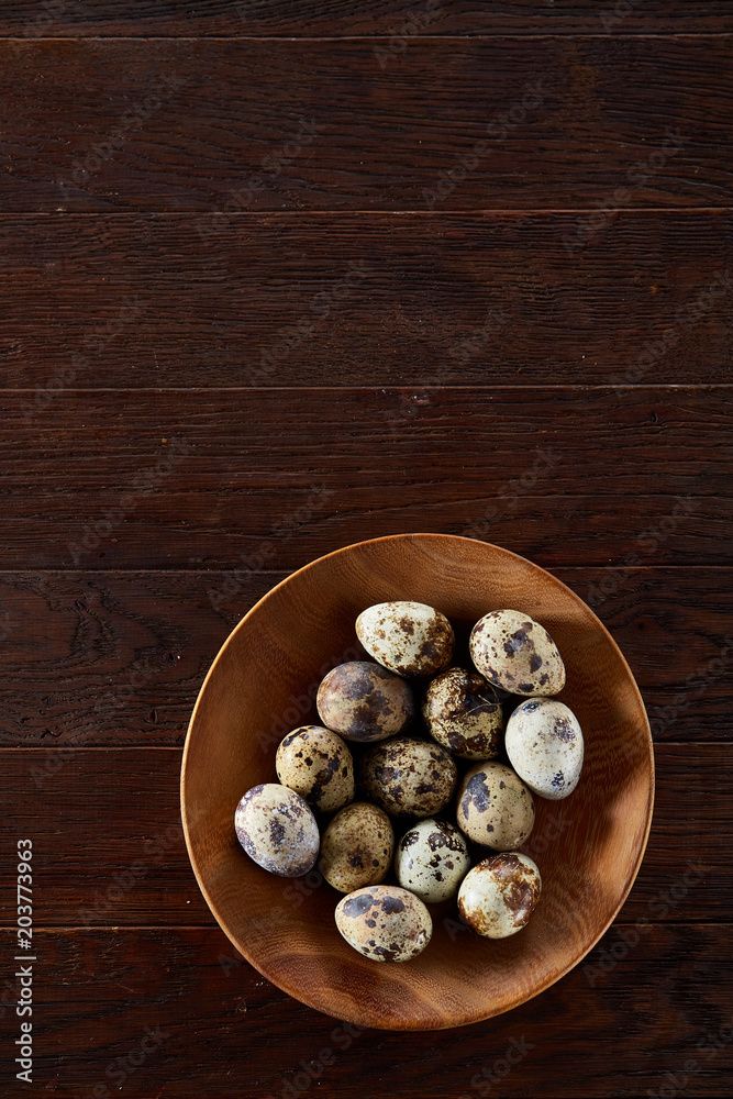 Fresh quail eggs in a wooden plate on a dark wooden background, top view, close-up Fresh quail eggs in a wooden plate on a dark wooden background, top view, close-up