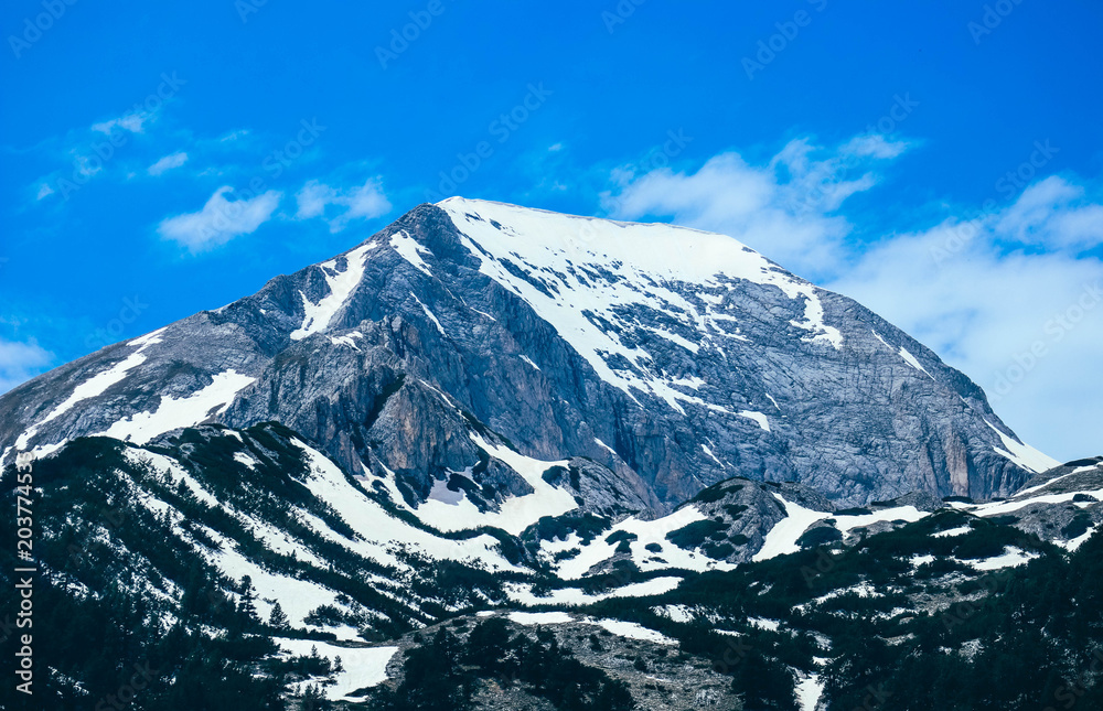 Mountain snow peak, beautiful natural winter backdrop. Ice top of the hill, blue sky background. Alpine forest landscape.