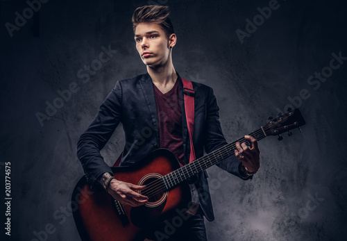 Stylish young musician with stylish hair in elegant clothes, playing on an acoustic guitar.