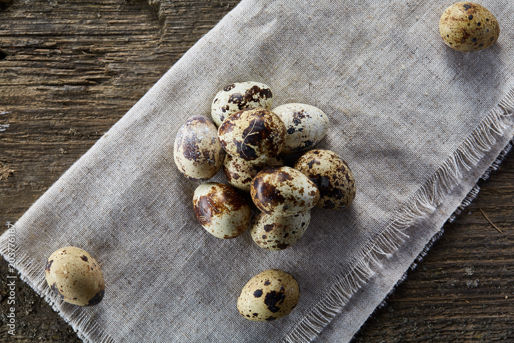 Quail eggs arranged in pyramid on a napkin with boxwood branches over a wooden table, close-up, selective focus. Quail eggs arranged in pyramid on a napkin with boxwood branches over a wooden table, close-up, selective focus.