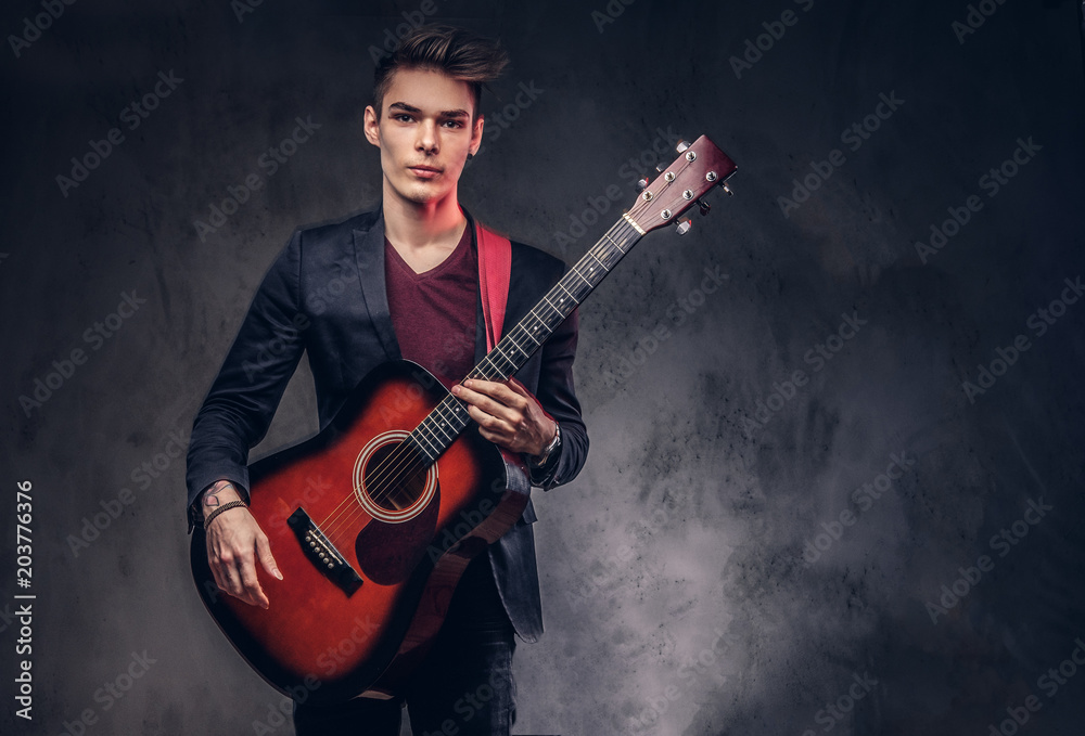 Obraz premium Stylish young musician with stylish hair in elegant clothes, playing on an acoustic guitar.