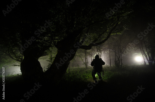 Night fog in the village. Mysterious. Lighting up Swing near the tree in the yard. The light from the backside of trees. Mystic night at countryside. Silhouette of man sitting on swing