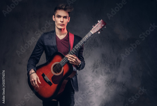 Stylish young musician with stylish hair in elegant clothes, playing on an acoustic guitar.