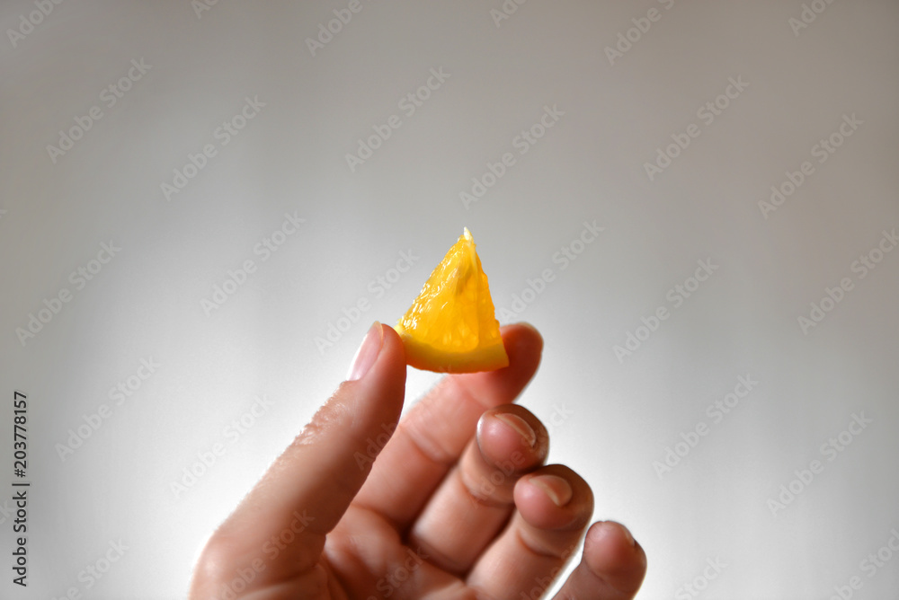 A small slice of orange in hands on a gray background. Orange in hand A small slice of orange in hands on a gray background. Orange in hand