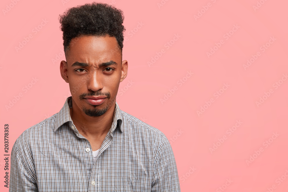 Moody dark skinned guy has trendy hairdo, sullen discontent expression, being in low spirit after quarrel with girlfriend, has some troubles, poses against pink background with blank copy space Moody dark skinned guy has trendy hairdo, sullen discontent expression, being in low spirit after quarrel with girlfriend, has some troubles, poses against pink background with blank copy space