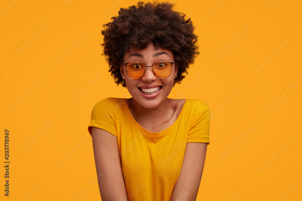 Portrait of glad cheerful African American female with positve expression, being in good mood after unforgettable journey with lover, isolated over yellow studio background. People, style, emotions Portrait of glad cheerful African American female with positve expression, being in good mood after unforgettable journey with lover, isolated over yellow studio background. People, style, emotions