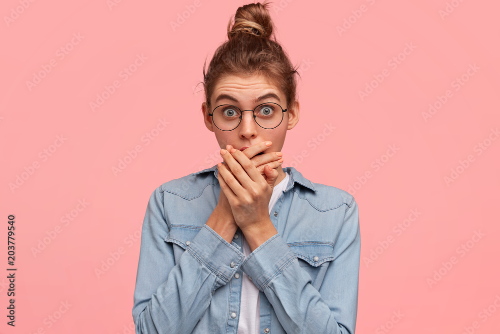 Horizontal shot of pretty young woman with terrified expression, covers mouth in bewilderment, feels embarrassed and shocked, recieves unexpected news, isolated on pink background. Reaction concept Horizontal shot of pretty young woman with terrified expression, covers mouth in bewilderment, feels embarrassed and shocked, recieves unexpected news, isolated on pink background. Reaction concept