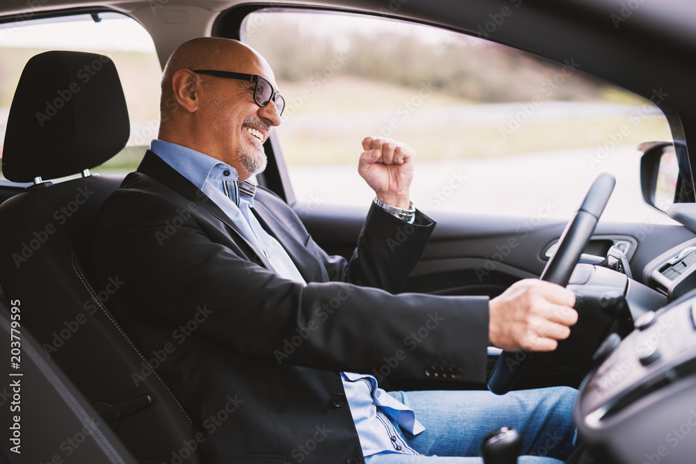 Mature cheerful professional elegant businessman in a suit is driving a car and laughing.