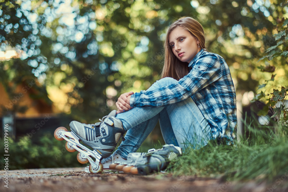 Beautiful woman in a fleece shirt and jeans resting after roller skating. Beautiful woman in a fleece shirt and jeans resting after roller skating.